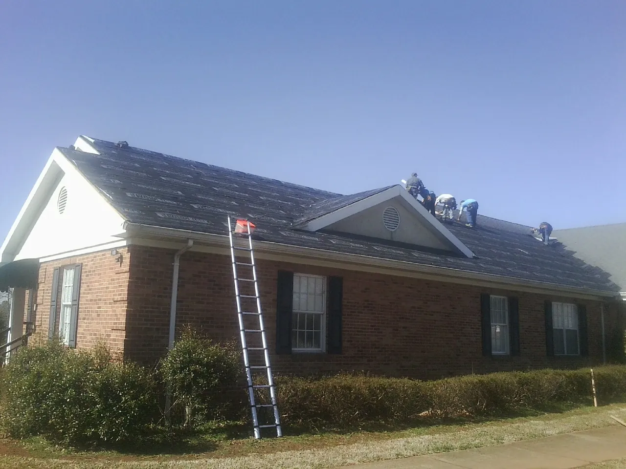 Crew tearing shingles off a brick ranch roof with a ladder set — Metal Roof Repair work by our crew in Pass Christian
