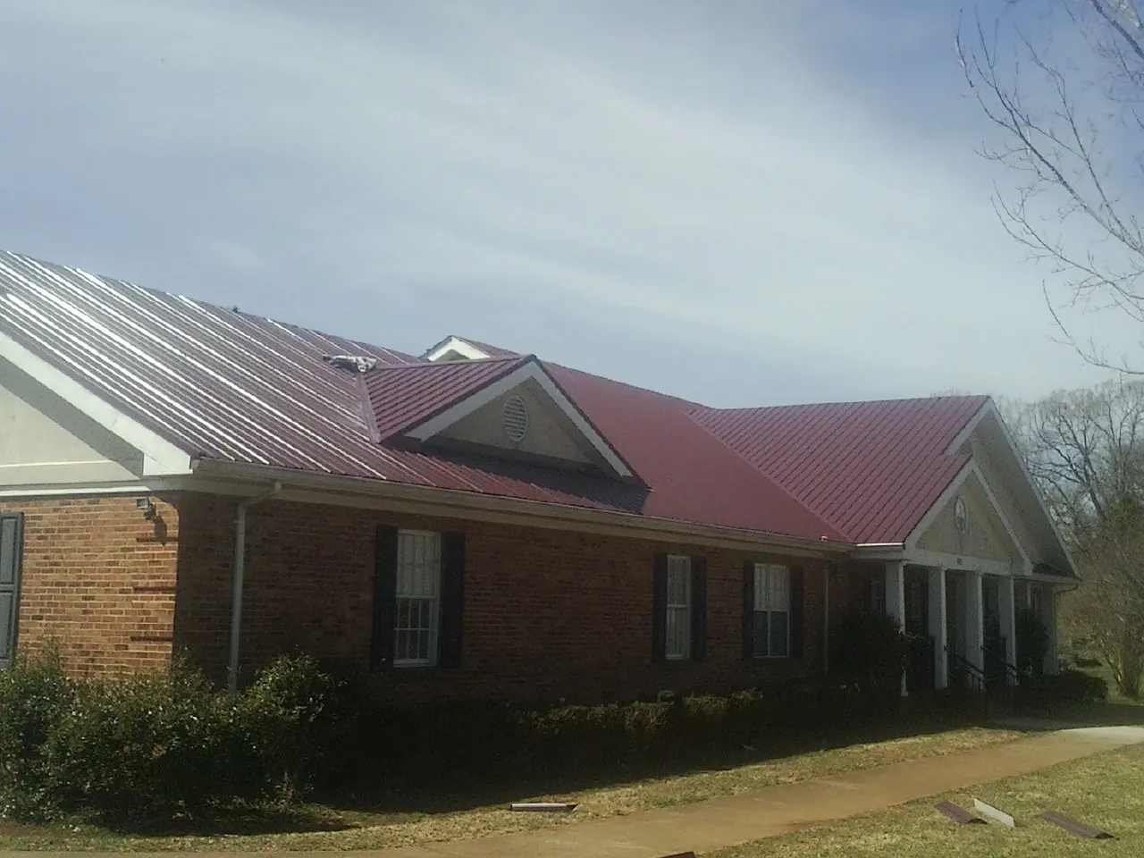 Red metal roof with gabled entries on a long brick building, from a Hail Damage Roof Repair job in Pass Christian