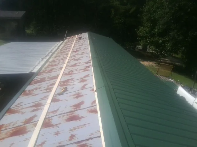 Old rusted panels beside newly installed green metal roofing — Wind Damage Roof Repair by Roofing Brothers in Pass Christian
