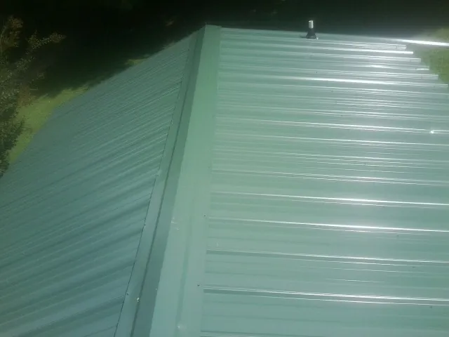 New green metal panels meeting at the ridge of a roof — Flat Roof Repair work by our crew in Pass Christian