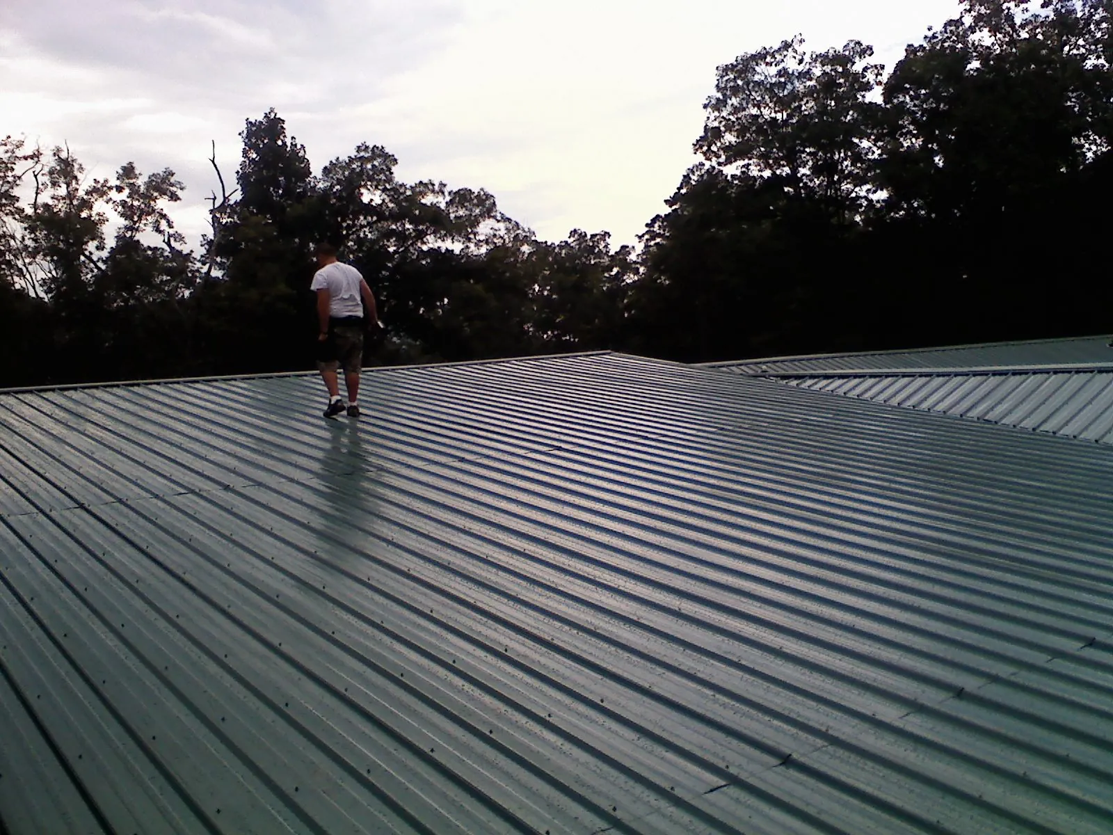 Roofer walking a wide expanse of new green metal roofing in Pass Christian