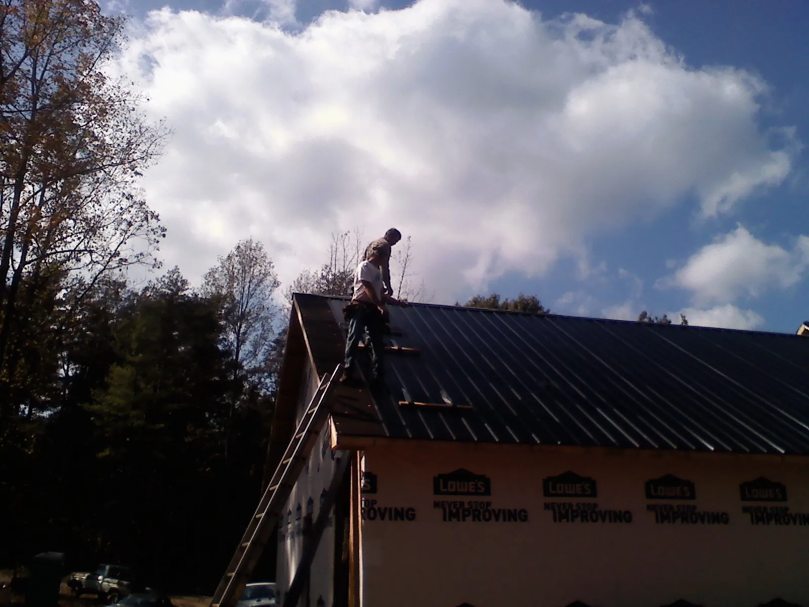 Roofer fastening dark metal panels high against a cloudy sky, from a Roof Inspection job in Pass Christian