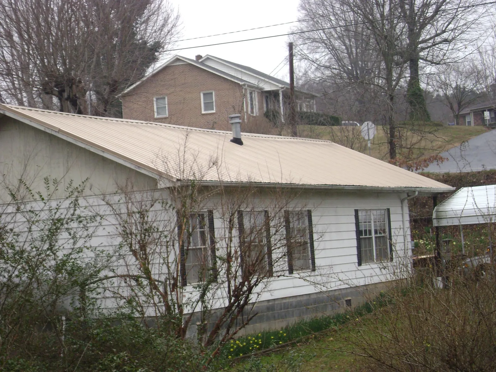 Tan metal roof on a white sided house set into a hillside — Commercial Roofing by Roofing Brothers in Pass Christian