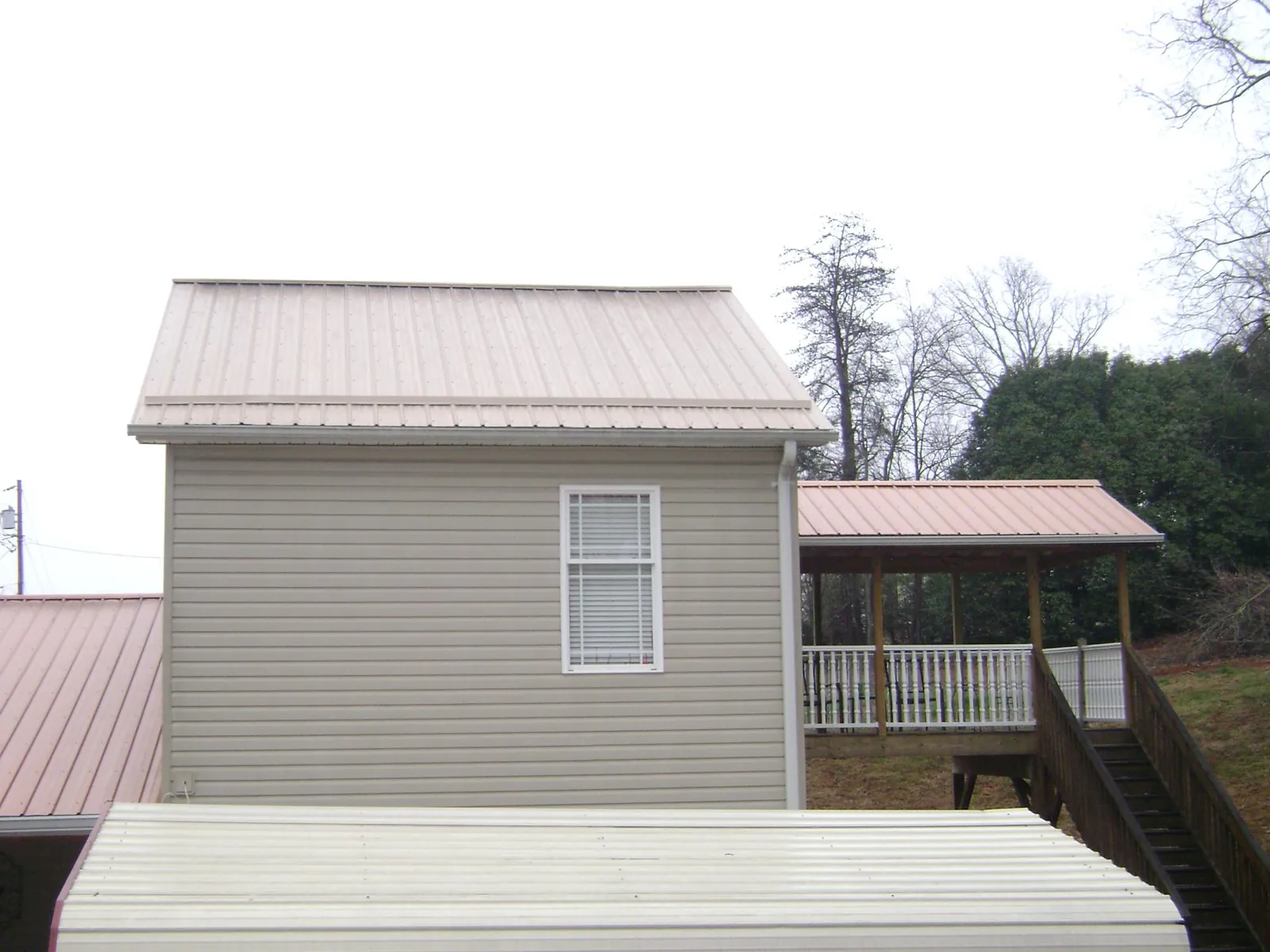 Tan metal roofs on a two story addition and attached porch, from a Roof Replacement job in Pass Christian